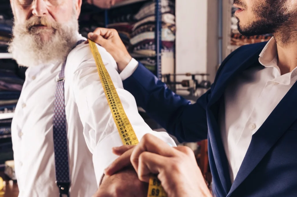 El sastre toma las medidas del brazo del cliente con una cinta métrica para su guía de tallas.