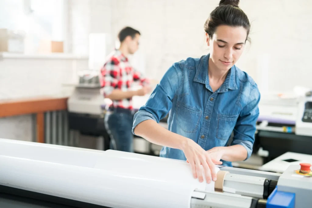 Mujer arrastrando la bobina de papel en un plotter de corte. 