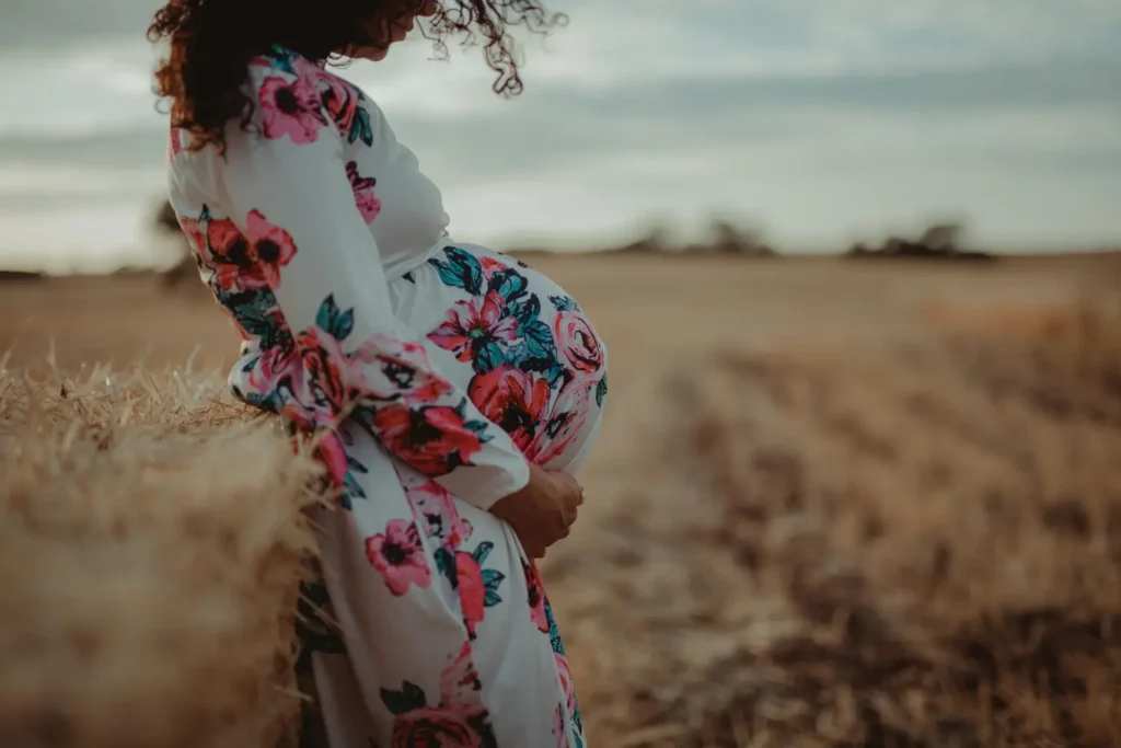 Mulher grávida usando um vestido branco com estampa floral, uma peça comum na moda gestante.