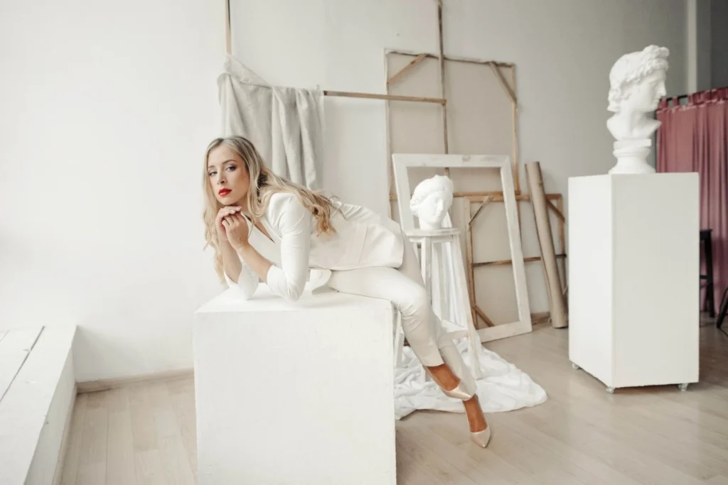 Donna vestita di bianco cloud dancer che posa in uno studio appoggiata a un cubo bianco