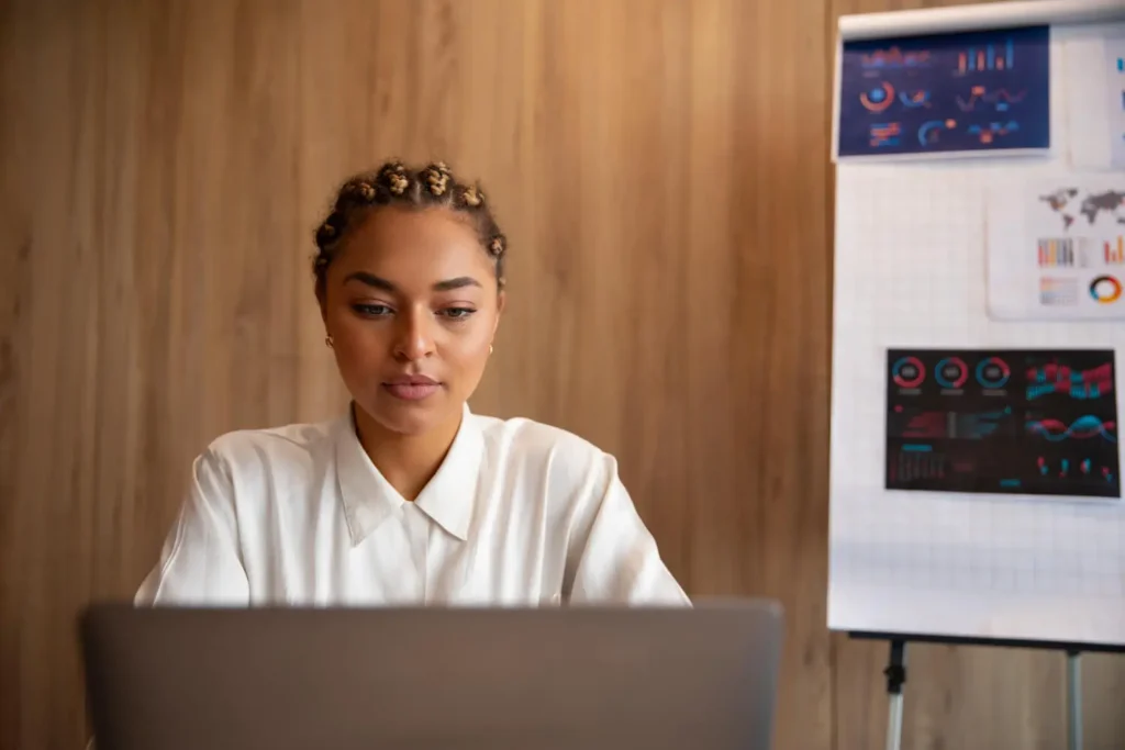 Gesti&oacute;n de producci&oacute;n: mujer en una computadora con gr&aacute;ficos al fondo