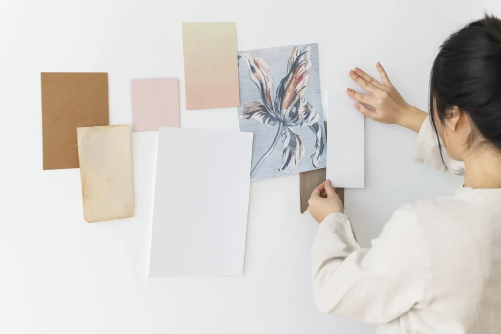 Una donna sta incollando su una parete dei fogli di carta di diversi colori e consistenze.