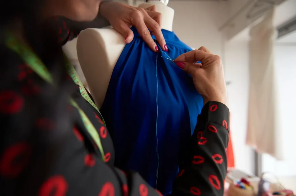 Algu&eacute;m costurando um vestido um vestido azul royal em um manequim. A costura &eacute; uma das principais etapas da cria&ccedil;&atilde;o de roupas.