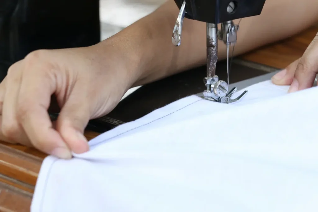 Algu&eacute;m costurando a bainha de uma camiseta clara com uma m&aacute;quina de costura.