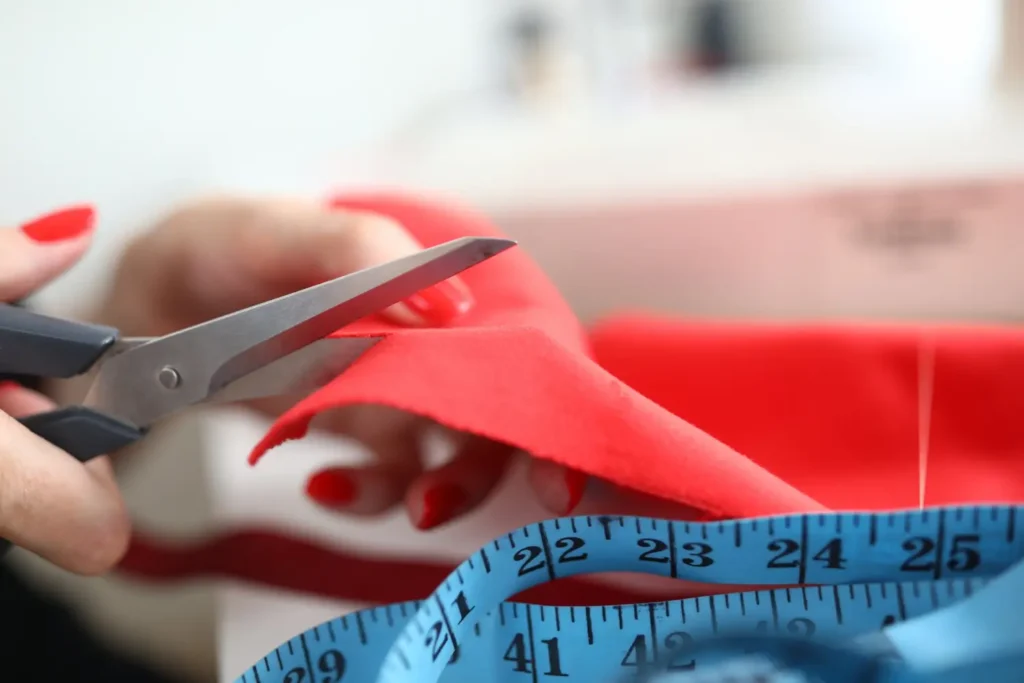 Profissional com tesoura e fita métrica cortando um tecido