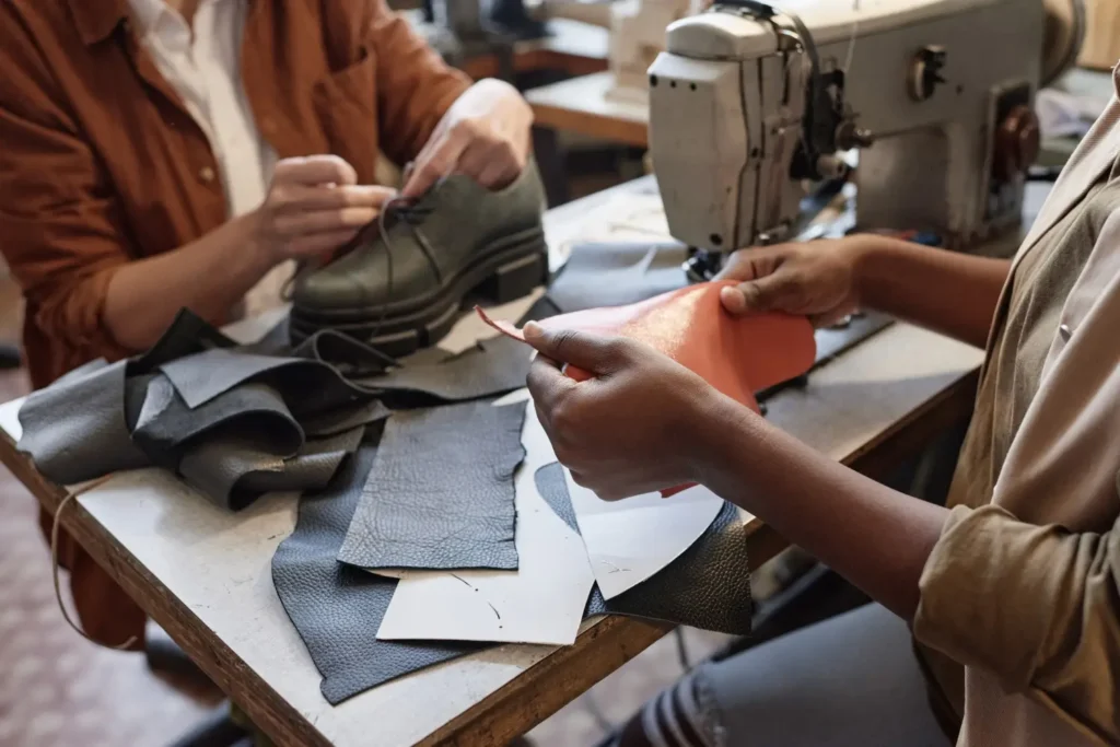 Dois profissionais de uma confec&ccedil;&atilde;o de moda terceirizada conferindo prot&oacute;tipo de sapato e peda&ccedil;os de tecido.